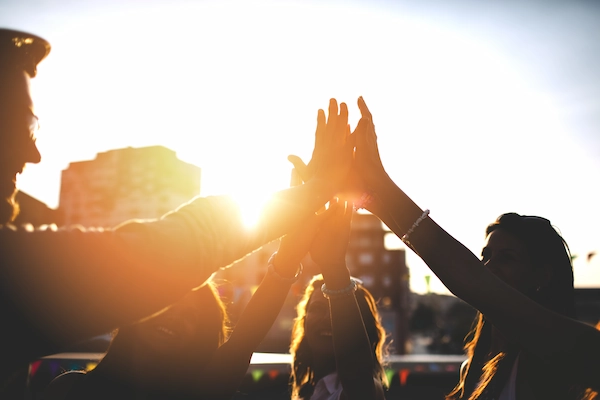 Groep mensen geeft elkaar een high five in de buitenlucht bij zonsondergang.