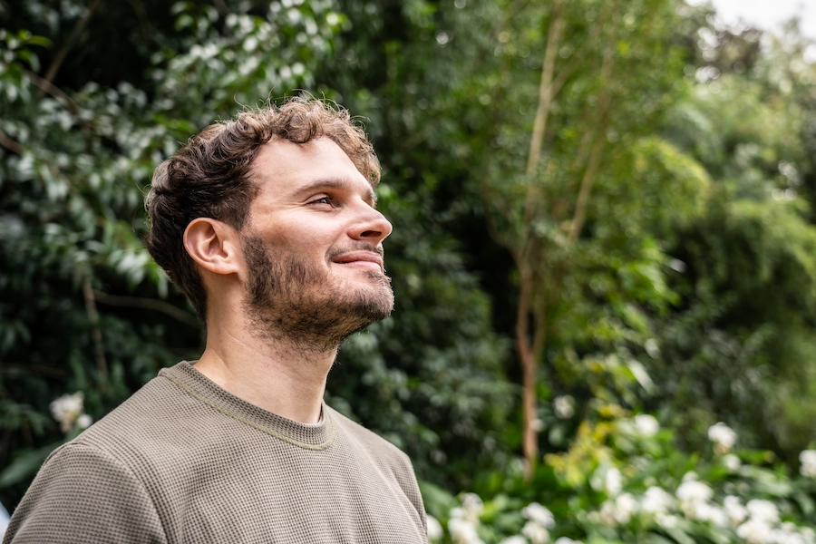 Jonge man kijkt met glimlach omhoog in een groen park.