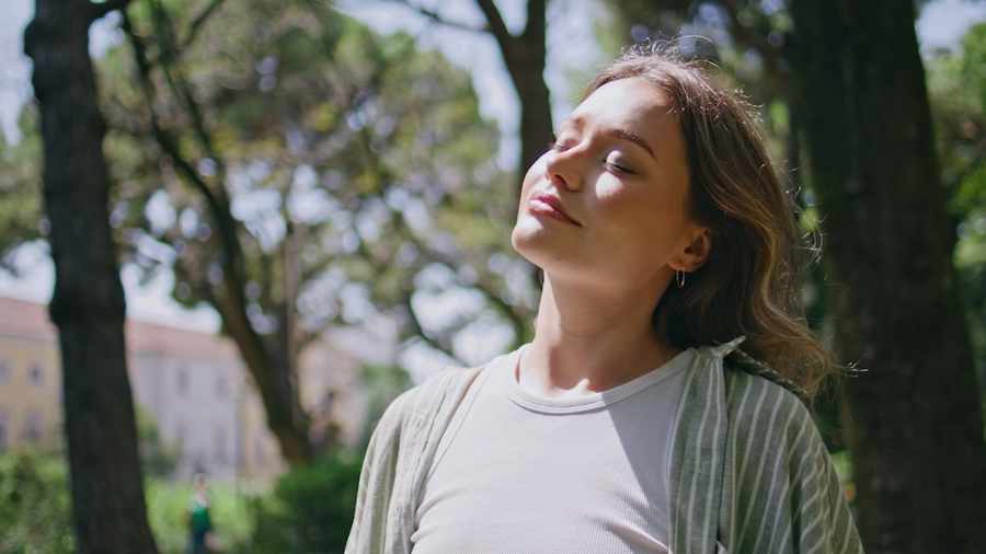 Jonge vrouw geniet ontspannen met gesloten ogen van de zon in een groene, bosrijke omgeving.