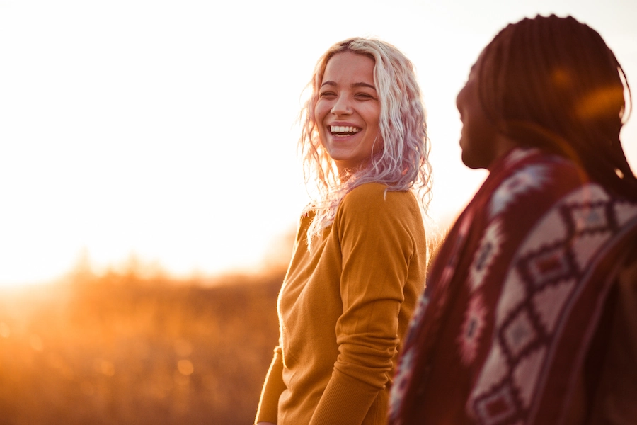 Twee vrouwen lachen samen in een zonovergoten veld tijdens zonsondergang.