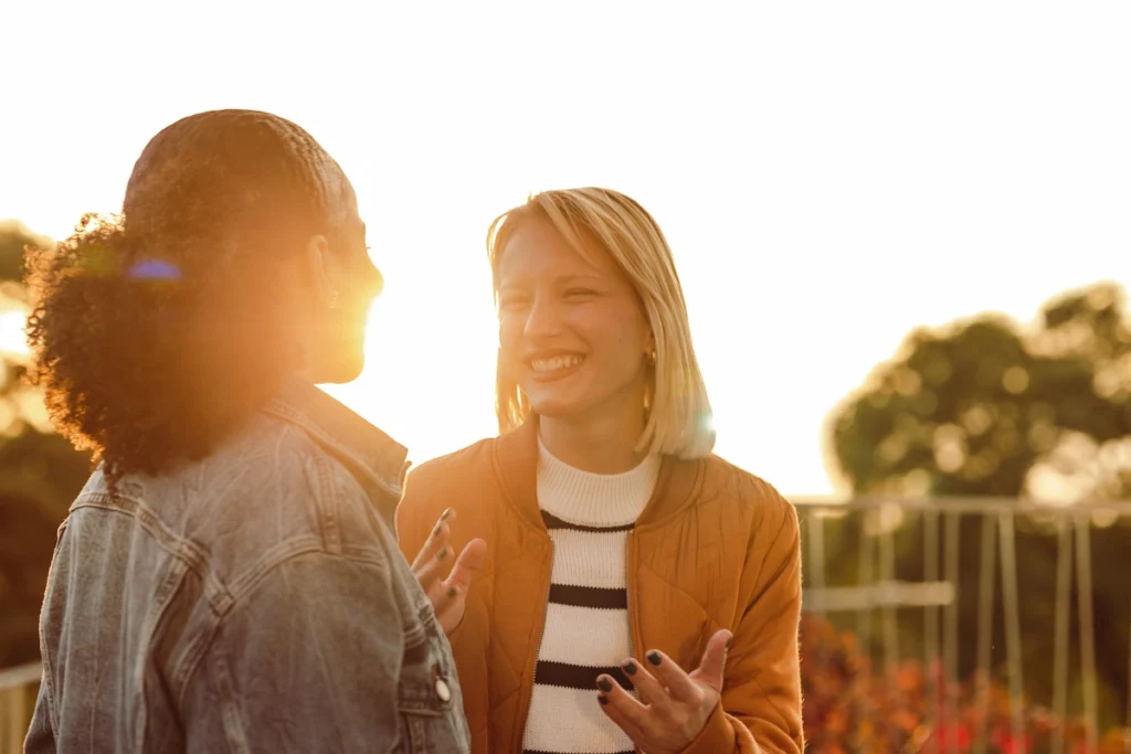 Twee vrouwen lachen en praten met elkaar buiten tijdens een ondergaande zon.