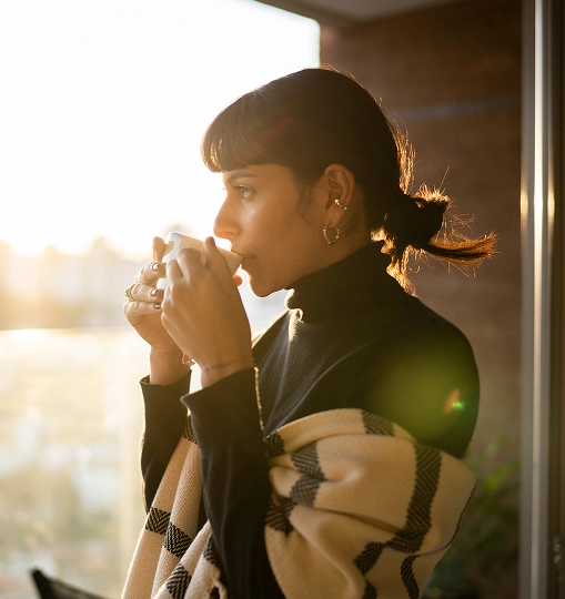 Vrouw drinkt koffie op een balkon tijdens zonsopgang.