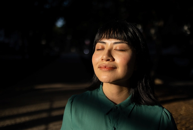 Vrouw met gesloten ogen geniet van de zon in een schaduwrijk park.