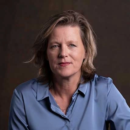 Portret van Janine Fidder van Happy Brain Clinics in een blauwe blouse tegen een donkere achtergrond.