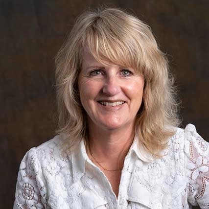 Portret van Margreet Top van Happy Brain Clinics, gekleed in een witte blouse voor een neutrale achtergrond.