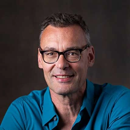 Portret van Reinout van Vliet van Happy Brain Clinics, met een glimlach en een blauwe overhemd.